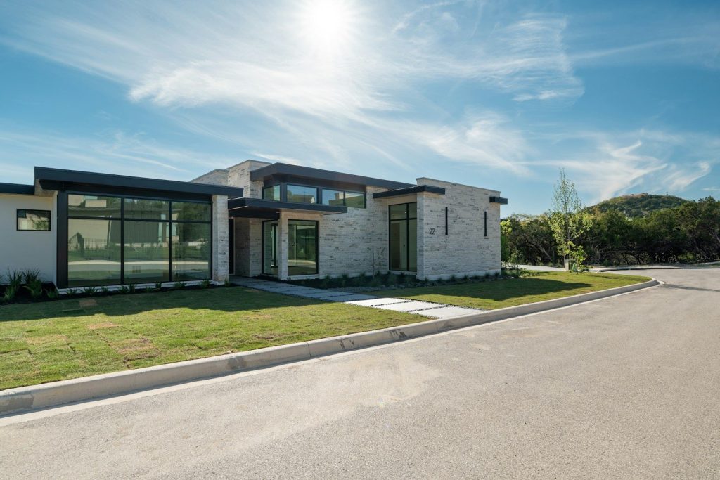 Modern stone house with large windows under a bright sky.